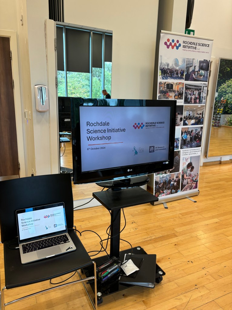 The initial set up of the session, with the screen displaying the first slide of the powerpoint, with the Rochdale Science Initiative banner behind it. 