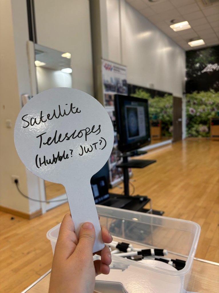 Max holding up a sign that says Space Telescopes as they participate in another speaker's session.